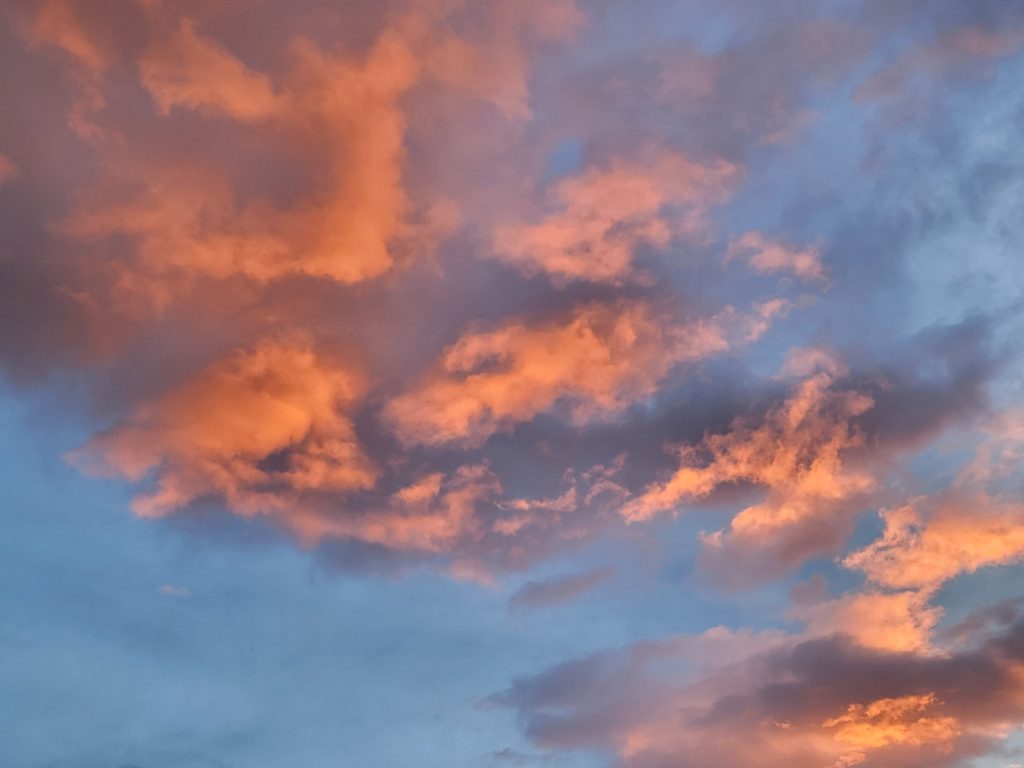 soft orange lights the base of the clouds at sunset with blue sky between.